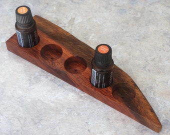 May include: Wooden essential oil holder with six slots. Two amber glass bottles with orange labels are in the holder. The labels read "Orange Peel" and "Lemon".