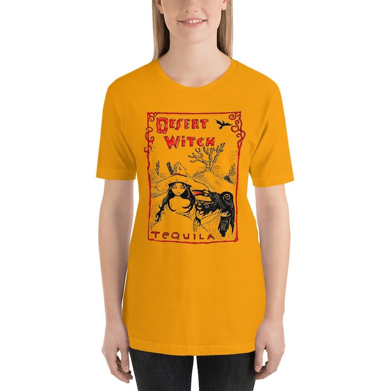 May include: A yellow t-shirt with a red and black graphic of a woman with a black bird on her shoulder. The graphic is in a rectangular frame with the text "Desert Witch Tequila" in red.