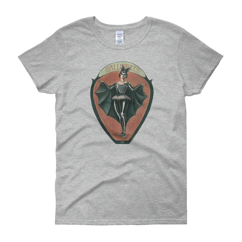 May include: A gray t-shirt with a vintage-style illustration of a woman in a bat costume. The illustration is surrounded by a red and orange oval with the word "HALLOWEEN" printed in black.