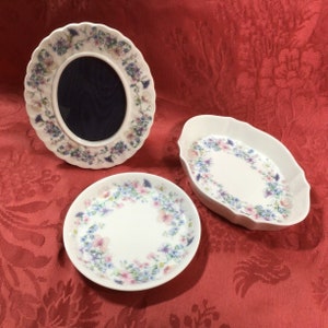 May include: Three white ceramic dishes with a floral pattern. The dishes are in the shape of a round plate, an oval dish, and a picture frame. The floral pattern is in shades of pink, blue, and green.