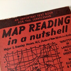 May include: A red book with the title "MAP READING in a nutshell" and the author's name "Major S. Bramley Moore, M.C (Author of Motor Vehicles in a Nutshell)". The book cover features a black and white map with a grid pattern.