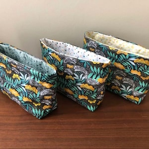 May include: Three fabric storage baskets with a black background and a floral pattern in shades of green, yellow, and white.