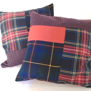 Peut inclure: Deux coussins décoratifs avec un motif patchwork. Les coussins sont faits de différents tissus à carreaux dans des tons de rouge, bleu, vert et jaune. Un coussin a un patch rouge uni au centre.