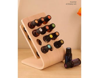 Puede incluir: Un expositor de madera para aceites esenciales con 15 ranuras para botellas. El expositor es de color marrón claro y tiene una base curva. Hay varias botellas de aceite esencial en el expositor, con etiquetas de diferentes colores.