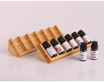 Puede incluir: Un soporte de madera con seis ranuras para sostener botellas de aceite esencial. El soporte está hecho de madera marrón claro y tiene una forma triangular. Seis botellas de aceite esencial se muestran en el soporte, con dos botellas más sentadas en la mesa frente al soporte.