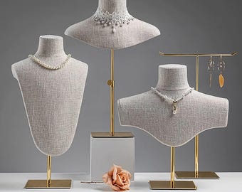 May include: Three gold metal necklace and earring display stands with fabric covered busts. The stands have square bases and adjustable heights. A single pink rose is in the foreground.