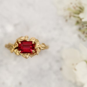 May include: A gold ring with a red gemstone set in a leafy design.