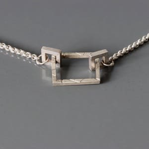 May include: A silver necklace with a square pendant made of interlocking geometric shapes.