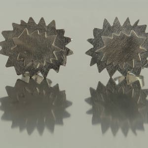 Puede incluir: Un par de pendientes de plata en forma de estrella con un diseño en capas.