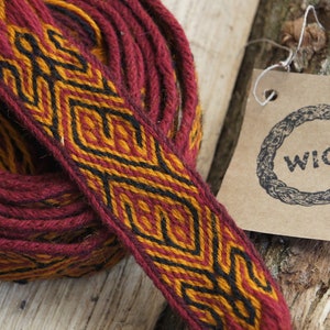 Könnte beinhalten: Gerolltes Textil in Burgunderrot, Gold und Schwarz mit geometrischem Muster. Ein Etikett mit dem Wort "WICI" ist angebracht. Das Textil wird wahrscheinlich für dekorative oder funktionelle Zwecke verwendet.