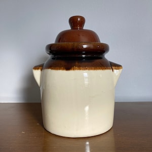 May include: A white ceramic jar with a brown lid. The jar has a brown band around the middle. The jar has two small handles on the sides.