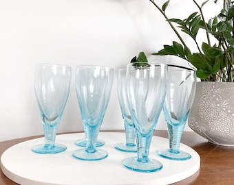 May include: Set of six light blue glass goblets with a delicate etched design. The goblets have a tall, slender shape with a rounded bowl and a flared base.