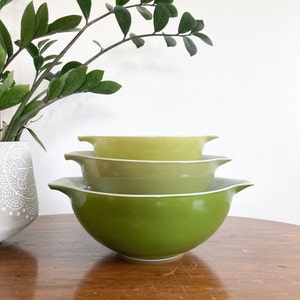 May include: A set of three green mixing bowls, nested together. The bowls are made of ceramic and have a glossy finish. The largest bowl is a bright green, the middle bowl is a light green, and the smallest bowl is a pale yellow.
