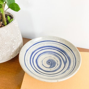 May include: A white ceramic bowl with a blue and white swirl design. The bowl is sitting on a book.
