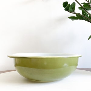 May include: An olive green mixing bowl with a white interior. The bowl has a wide rim and a smooth, glossy finish. The bowl is on a white surface. The bowl is suitable for mixing ingredients.