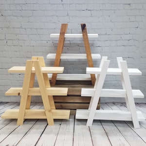 May include: Three wooden A-frame shelves, one natural wood, one stained brown, and one white. Each shelf has three tiers.