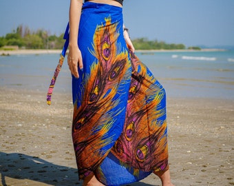 Puede incluir: Falda envolvente azul vibrante con diseño de plumas de pavo real en tonos naranja, amarillo y rosa. La falda se ata a la cintura con una faja a juego. La modelo lleva un top negro sin tirantes. Ideal para la playa.