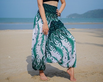 May include: A woman wearing a black tank top and green and white printed pants with a paisley pattern. She is standing on a sandy beach with the ocean in the background.