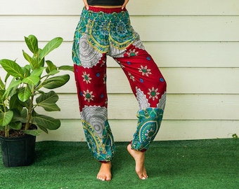 Puede incluir: Pantalones harem estampados con diseños en rojo, turquesa y blanco. Los pantalones tienen cintura elástica y se combinan con un top corto negro y un sombrero de paja. Presentan un estampado floral y paisley.