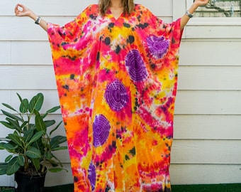 Może przedstawiać: Długa, zwiewna sukienka kaftan w stylu tie-dye w odcieniach pomarańczowego, różowego, fioletowego i czarnego. Sukienka ma dekolt w kształcie litery V i jest wykonana z lekkiej tkaniny.