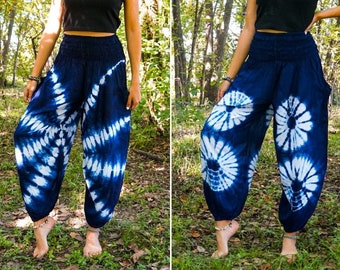 May include: A person wearing a black tank top and blue and white tie-dye pants. The pants have a wide leg and a loose fit. The person is standing in a forest setting.