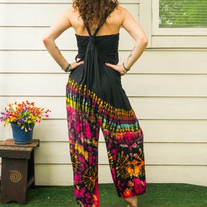 May include: A woman wearing a black halter top and tie-dye pants with pink, orange, yellow, and blue colors. The pants have a wide leg and a loose fit.