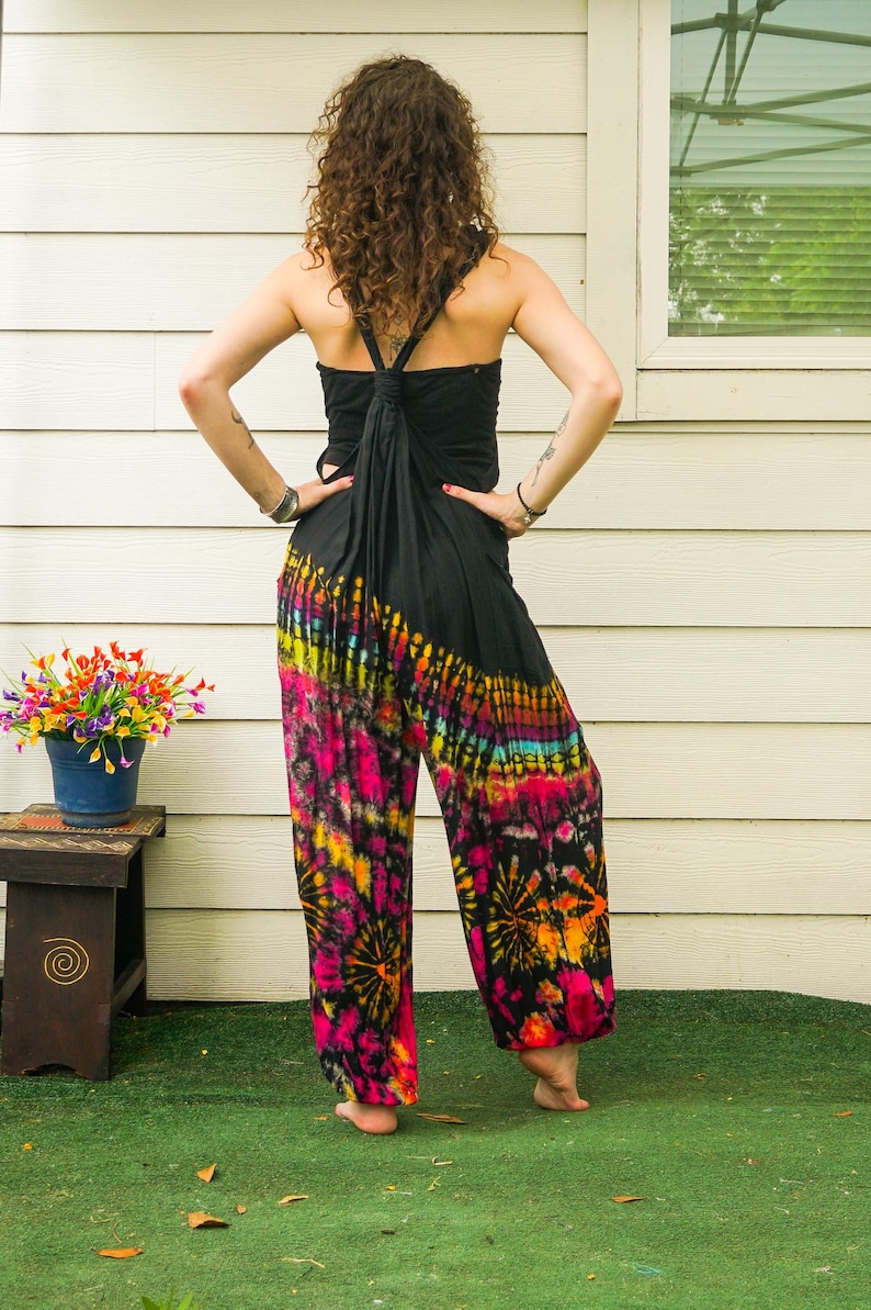 May include: A woman wearing a black halter top and tie-dye pants with pink, orange, yellow, and blue colors. The pants have a wide leg and a loose fit.