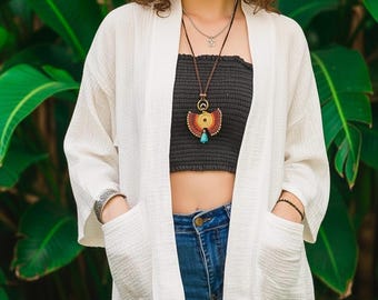 Puede incluir: Un cárdigan blanco abierto por delante con mangas tres cuartos y dos grandes bolsillos frontales, usado sobre un top negro sin tirantes y pantalones vaqueros azules, con un collar de varias capas con un colgante circular y una pulsera ancha.