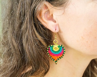 May include: A vibrant, heart-shaped earring with a gold-coloured hook. The earring has a spiral design at the top and is decorated with a rainbow of colours, including green, blue, pink, and orange. Small gold beads line the edges.