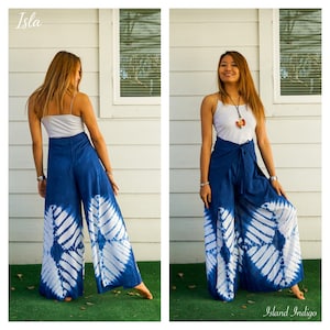 May include: A pair of wide-leg trousers featuring a deep blue and white tie-dye pattern with a diamond-shaped motif. The trousers have a high-waisted design with a tie-front closure. The text Isla and Island Indigo appear in the corners.