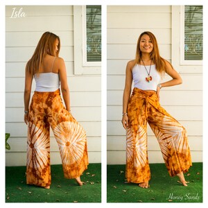May include: Wide-leg pants featuring a brown and white tie-dye sunburst pattern. The pants have a high-waisted design with a tie-front closure. The fabric displays a repeating circular motif in shades of burnt orange and white throughout the garment.