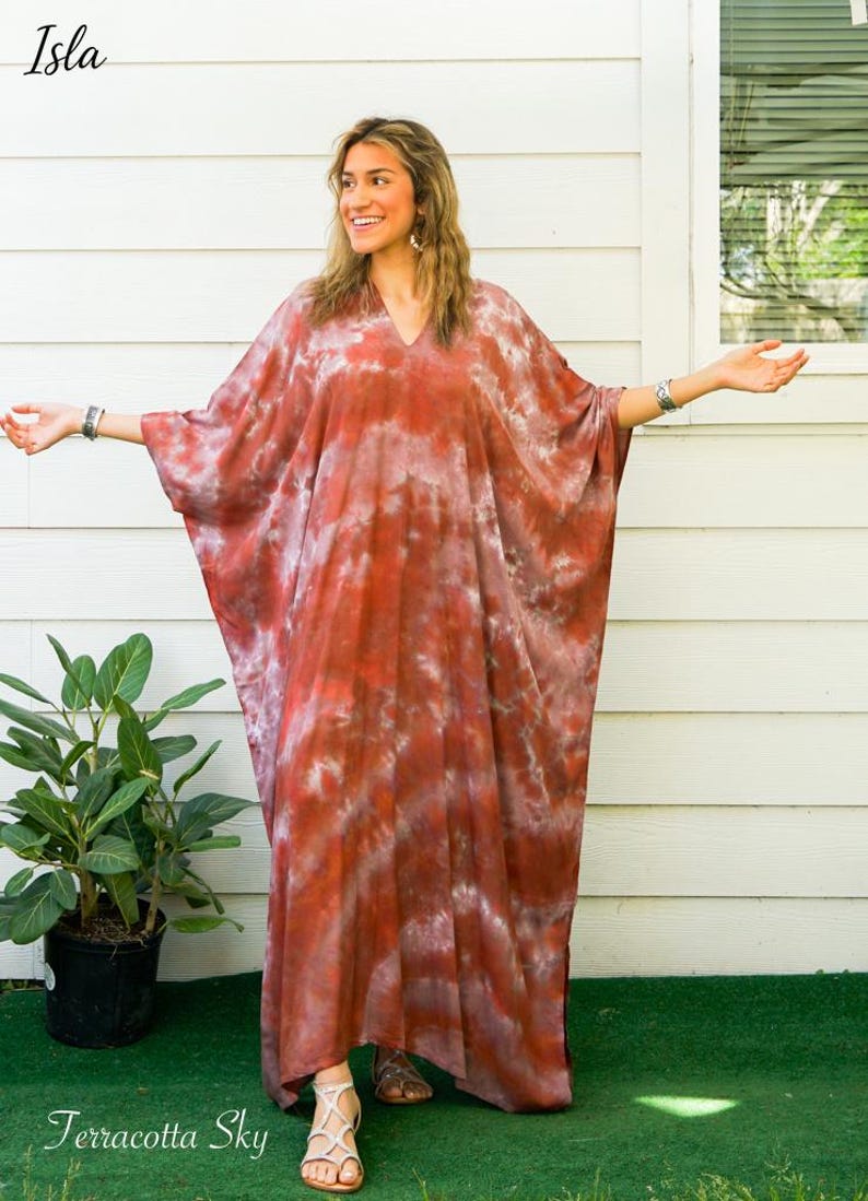 Op de afbeelding: Een enkellange kaftan-jurk met een tie-dye patroon in tinten terracotta, roest en wit. Het kledingstuk heeft een V-hals, wijde vloeiende mouwen en een los, ontspannen silhouet. De tekst Isla en Terracotta Sky zijn zichtbaar in de afbeelding.
