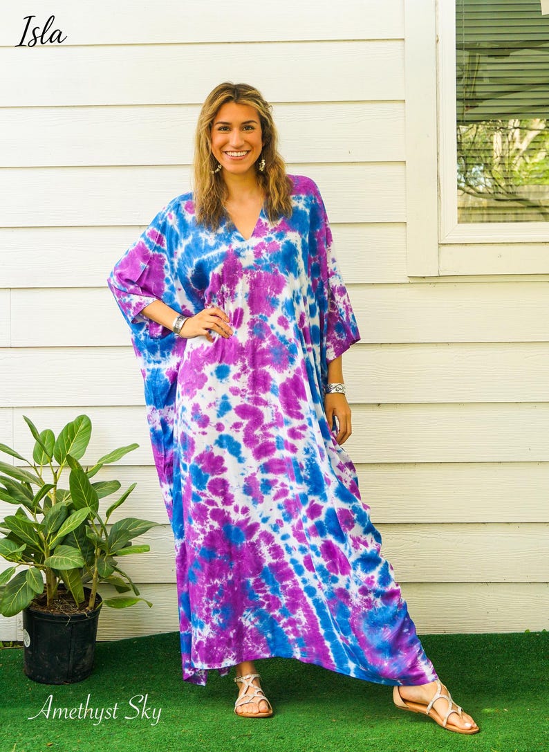 Op de afbeelding: Een enkellange kaftan met een levendig tie-dye patroon in tinten helderblauw, dieppaars en wit. Het kledingstuk heeft een V-hals, wijde mouwen en een losvallend silhouet. De tekst Isla en Amethyst Sky zijn in de afbeelding zichtbaar.