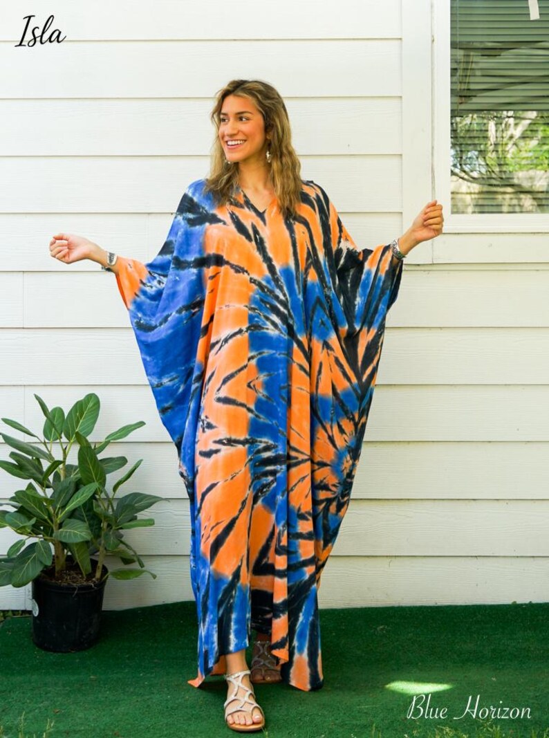 Op de afbeelding: Een vloerlange kaftan met een levendig tie-dye patroon in tinten feloranje, diepblauw en zwart. Het kledingstuk heeft een V-hals, wijd uitlopende mouwen en een losvallend silhouet. De tekst "Isla" en "Blue Horizon" is in de afbeelding aanwezig.
