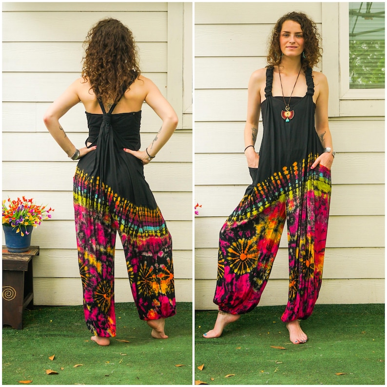 May include: A black tie-dye jumpsuit with a colorful floral pattern. The jumpsuit has a halter top with a criss-cross strap design and a wide leg.