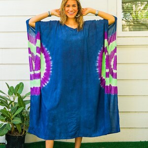 Op de afbeelding: Een ruimvallende kaftan-jurk in diep indigoblauw met een levendig tie-dye patroon aan de zijkanten met concentrische cirkels in felpaars en limoengroen. Het kledingstuk heeft wijde mouwen en een eenvoudige halslijn, gelabeld met Isla en Indigo Orchid.