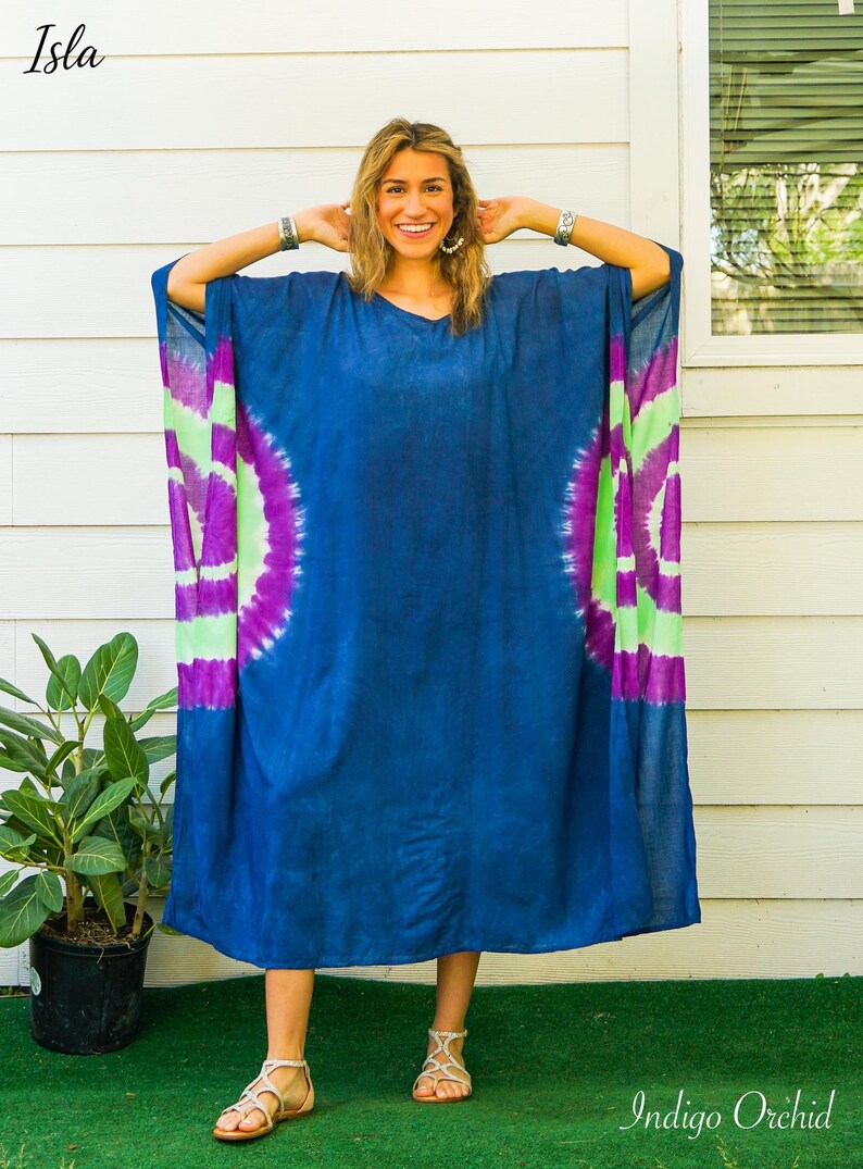 Op de afbeelding: Een ruimvallende kaftan-jurk in diep indigoblauw met een levendig tie-dye patroon aan de zijkanten met concentrische cirkels in felpaars en limoengroen. Het kledingstuk heeft wijde mouwen en een eenvoudige halslijn, gelabeld met Isla en Indigo Orchid.