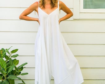 May include: A solid white sleeveless jumpsuit featuring a V-neckline, thin shoulder straps, and a loose, wide-leg silhouette that falls to a cropped length. The garment is constructed from a lightweight fabric with a relaxed, flowing fit.