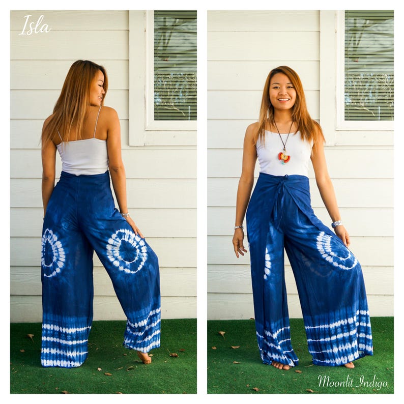 May include: Wide-leg pants in deep indigo blue featuring a white tie-dye circular pattern on each leg and a horizontal striped tie-dye design at the hem. The pants have a high-waisted wrap-style front with a tie closure at the center waist.