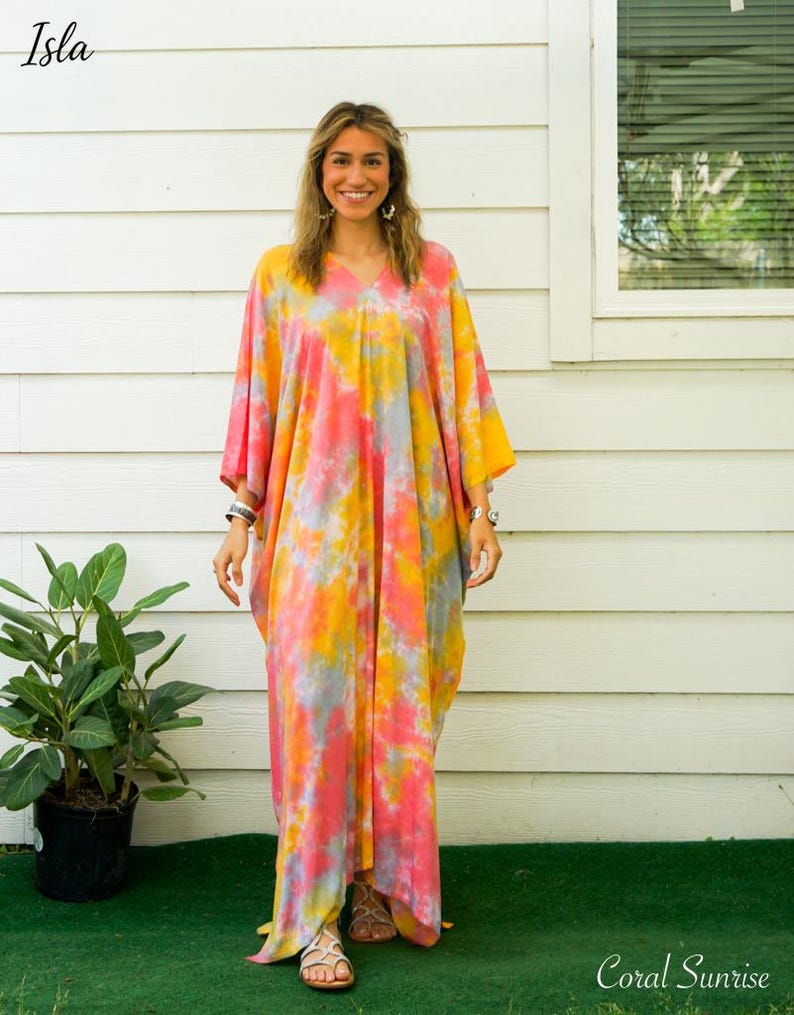 Op de afbeelding: Een enkellange kaftan-jurk met een levendig tie-dye patroon in tinten koraalroze, felgeel en zachtgrijs. Het kledingstuk heeft een V-hals, wijde mouwen en een losvallend silhouet dat tot aan de enkels reikt.