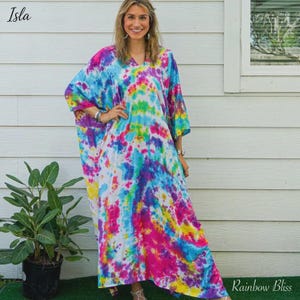 Op de afbeelding: Een vloerlange kaftanjurk met een levendig tie-dye patroon in tinten felblauw, magenta, geel en groen. Het kledingstuk heeft een V-hals, losse korte mouwen en een ontspannen, vloeiend silhouet dat tot aan de enkels reikt.