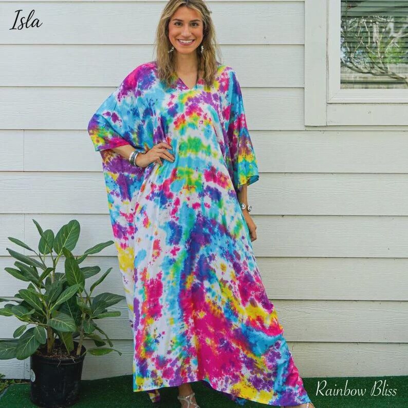 Op de afbeelding: Een vloerlange kaftanjurk met een levendig tie-dye patroon in tinten felblauw, magenta, geel en groen. Het kledingstuk heeft een V-hals, losse korte mouwen en een ontspannen, vloeiend silhouet dat tot aan de enkels reikt.