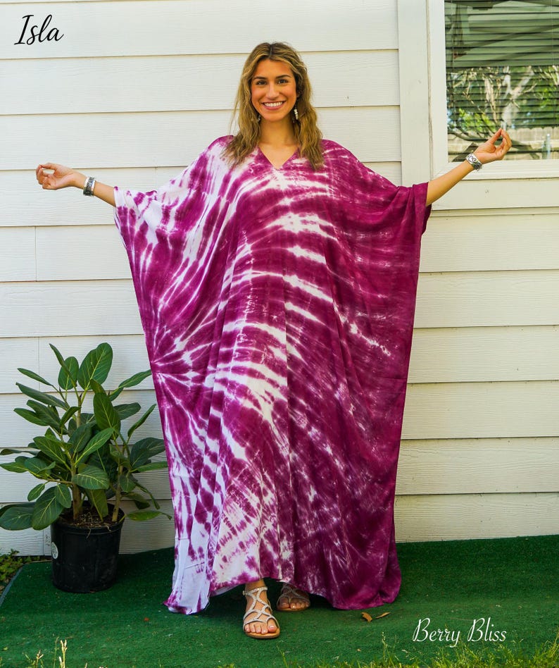 Op de afbeelding: Een vloerlange kaftan met een levendig magenta en wit tie-dye patroon, voorzien van een V-hals en wijde, vloeiende mouwen. Het kledingstuk toont een stralend spiraalontwerp dat zich over de stof uitstrekt voor een opvallend contrast.