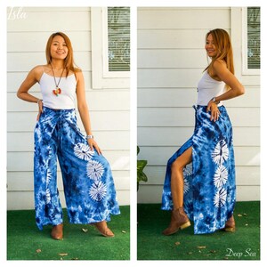 May include: A white spaghetti strap tank top paired with wide-leg pants featuring a blue and white tie-dye pattern. The pants have a high-waisted design with a tie closure and vertical side slits that reveal a series of circular white motifs.