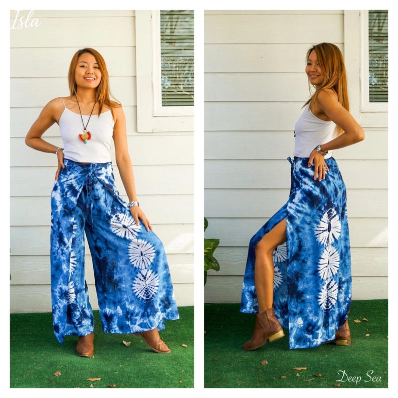 May include: A white spaghetti strap tank top paired with wide-leg pants featuring a blue and white tie-dye pattern. The pants have a high-waisted design with a tie closure and vertical side slits that reveal a series of circular white motifs.