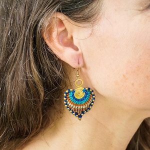 May include: A pair of gold-toned earrings with a heart-shaped design. The earrings are made of small blue, orange, and brown beads.