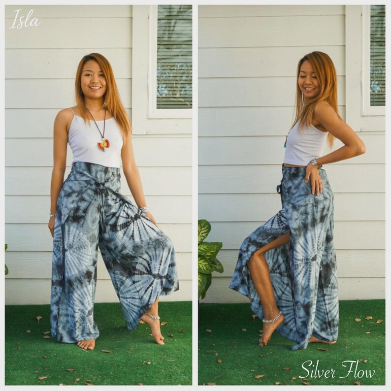 May include: A white tank top paired with wide-leg pants featuring a blue and black tie-dye pattern. The pants have a high-waisted design with a tie closure at the front and side slits that reveal the legs. The text Isla and Silver Flow appear.