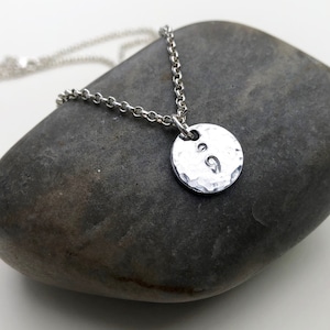 Puede incluir: Collar de plata con un colgante de plata martillado con un símbolo de punto y coma.
