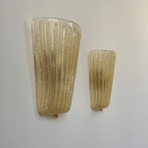 May include: Two wall sconces with a textured, ribbed design in a warm amber color. The sconces are mounted on a white wall and have a gold-colored base.