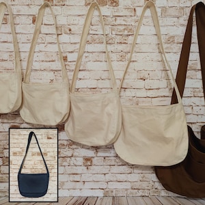 May include: A collection of canvas crossbody bags in off-white and brown, featuring a long shoulder strap and a rounded bottom. An inset image shows a single dark blue crossbody bag with a flap closure and a long shoulder strap.